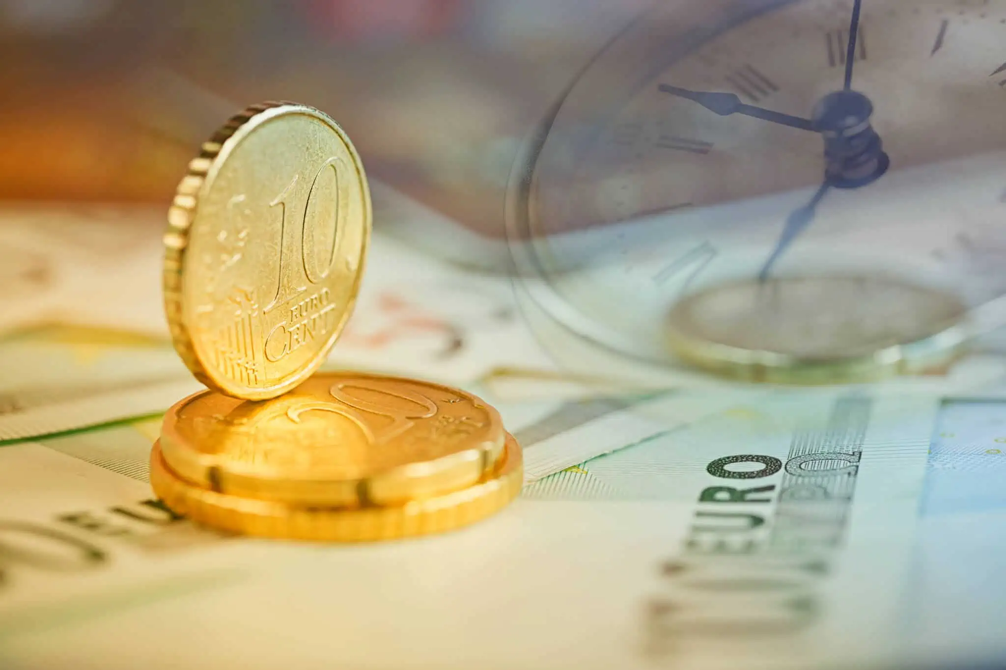 Taxa de juro nominal, real e efetiva: Quais as diferenças? Moedas de euro empilhadas em cima de notas de euro, numa alusão à poupança e ao investimento