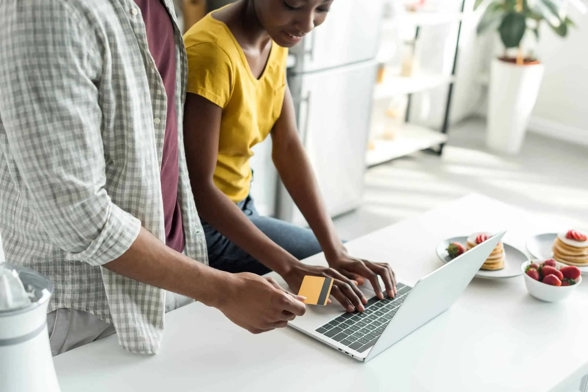Comparar preços online: 12 sites que podem ajudar pai e filha adolescente na bancada da cozinha estão a consultar computador portátil para comparar preços online, e pagar com o cartão que estão a segurar