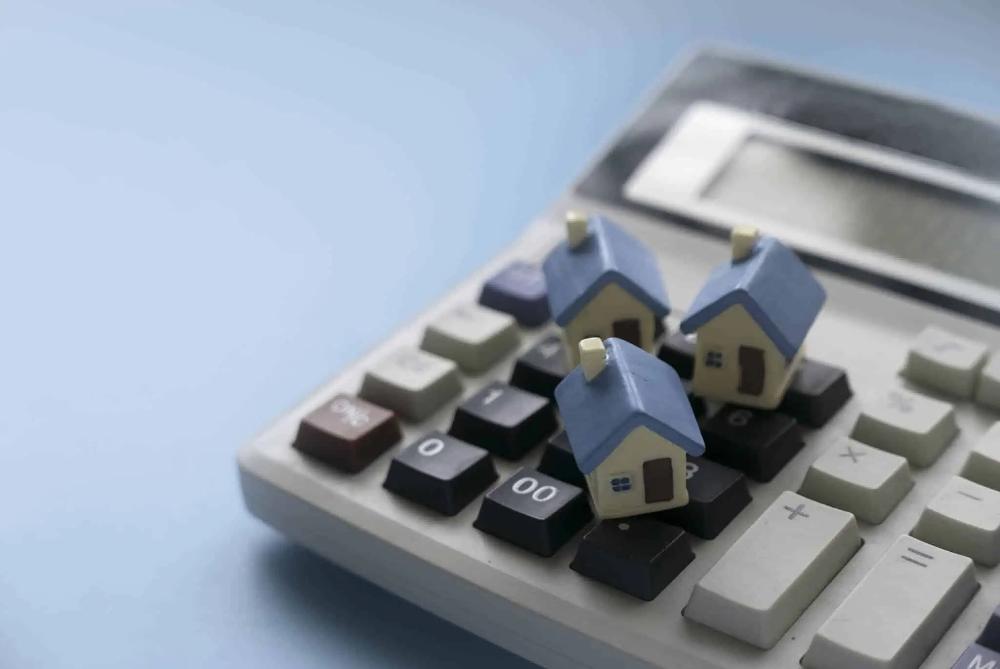 Quantas vezes posso renegociar o meu crédito habitação? imagem de uma calculadora com várias casas em miniatura em cima numa alusão à renegociação e transferência de crédito habitação
