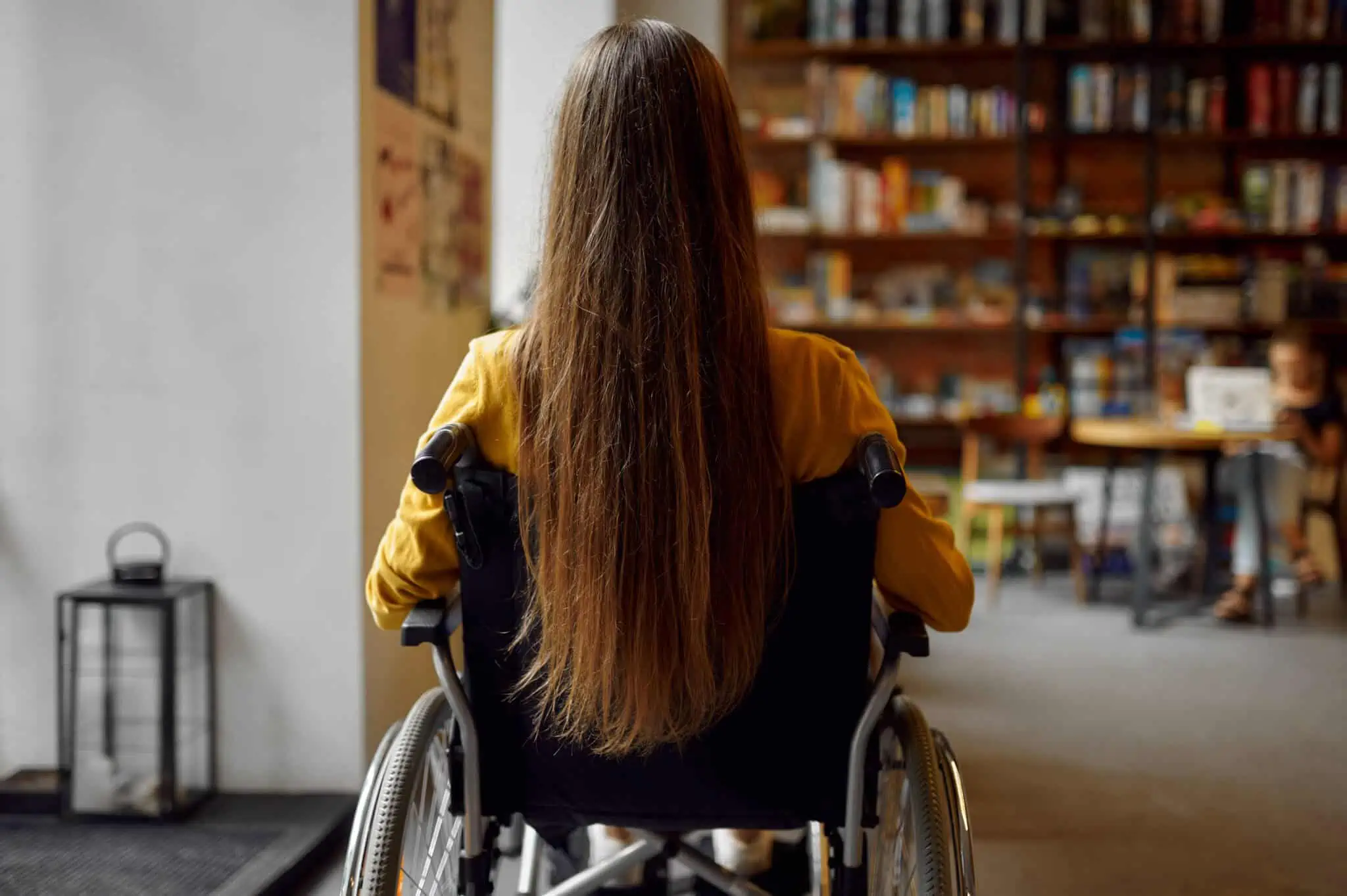 Incapacidade motora: Como pedir o atestado multiuso e o dístico adolescente em cadeira de rodas, portadora de atestado multiuso e o dístico, numa sala de biblioteca cheia de livros