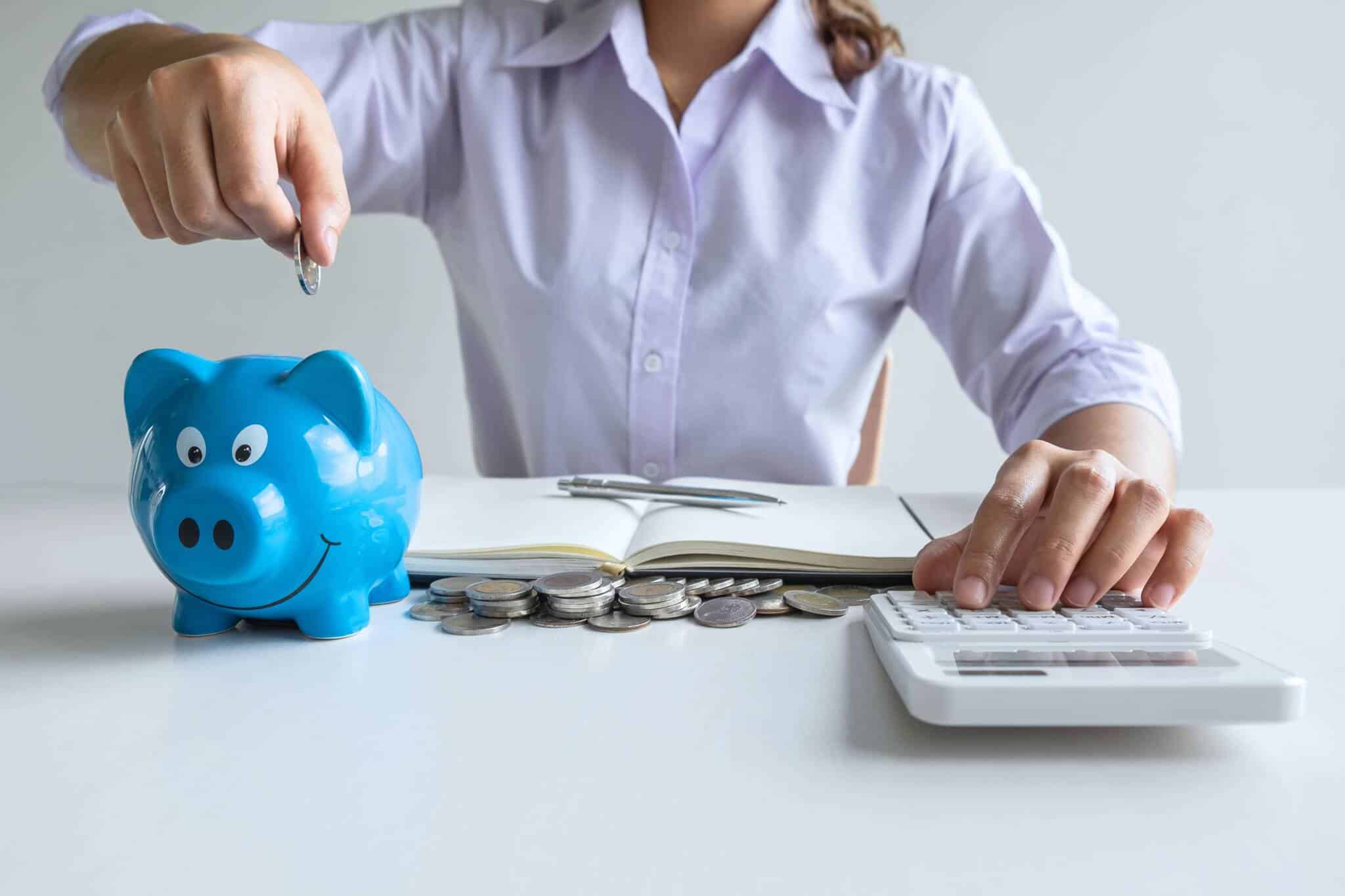 Mulher a fazer contas e a colocar moedas num porquinho mealheiro a ilustrar que está a analisar as possibilidades de transferências de PPR para produtos mais vantajosos