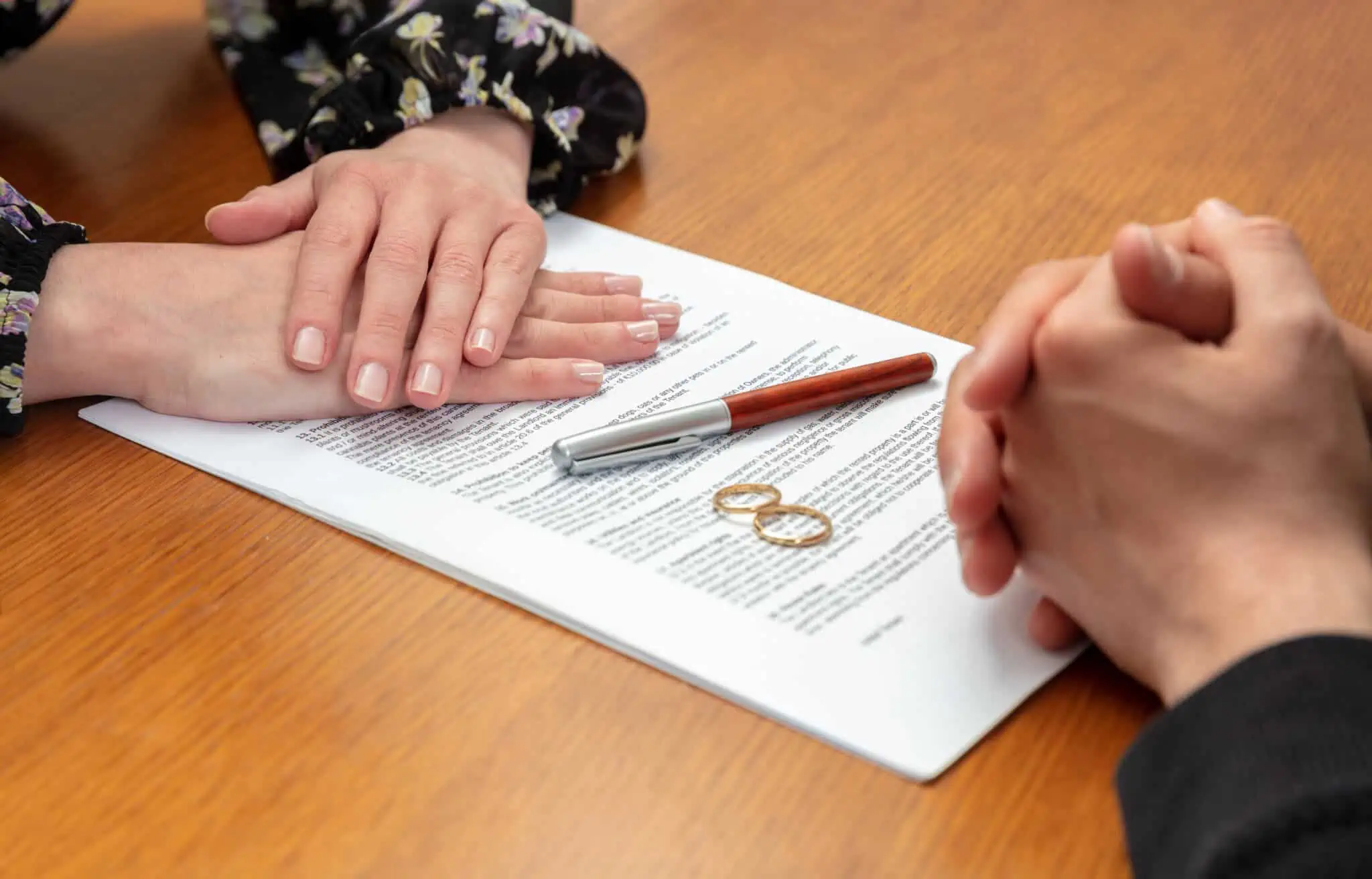 Regime de casamento com separação total de bens: Como funciona? mãos de um casal frente a frente, sob um documento , junto a umas alianças, e com uma caneta para assinar após a decisão de escolher entre a união de facto e casamento