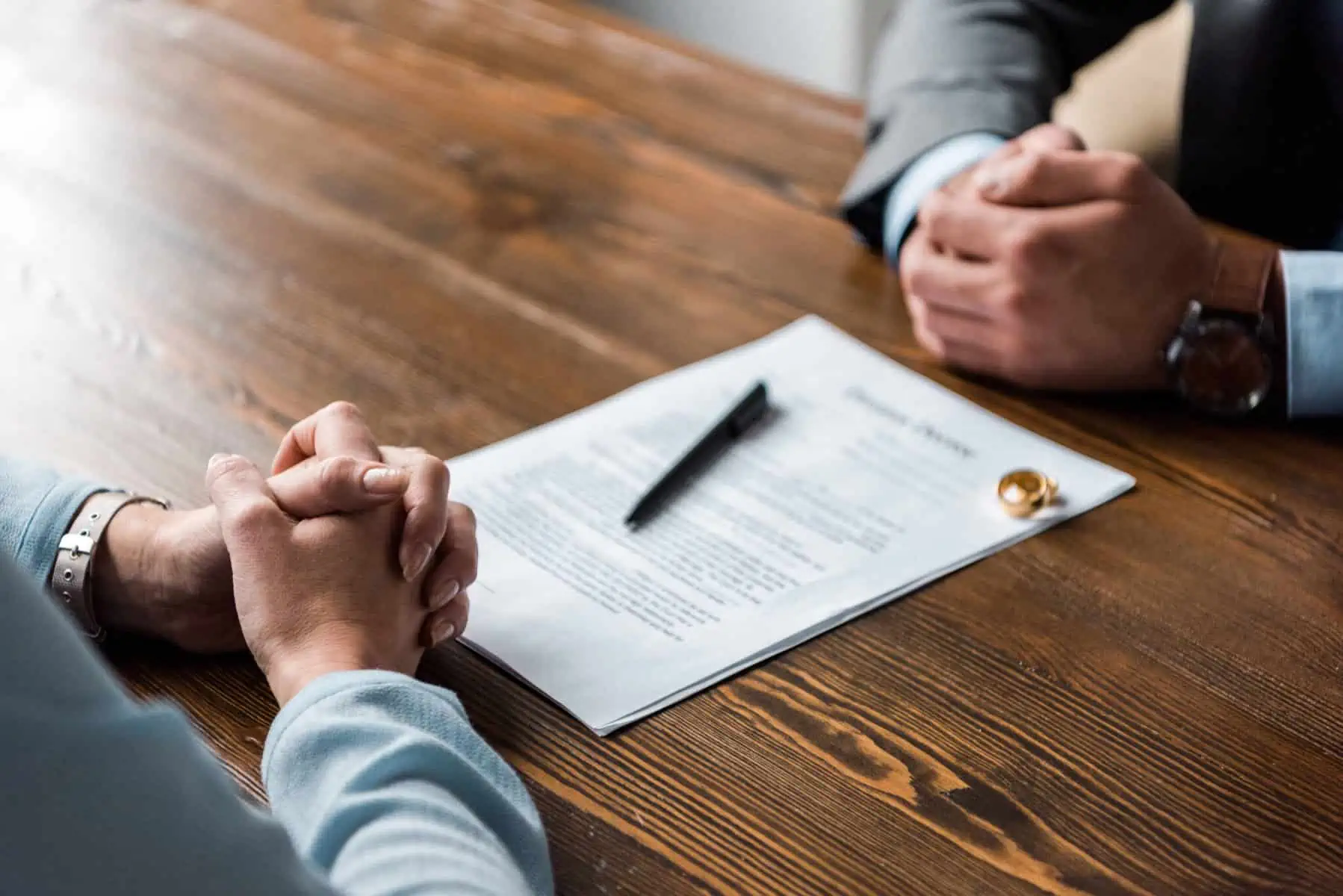 Posso iniciar um processo de divórcio sem advogado? mãos cruzadas de duas pessoas em cima de um acordo que vão assinar, com as alianças ao pé, aceitando avançar com divórcio sem advogado