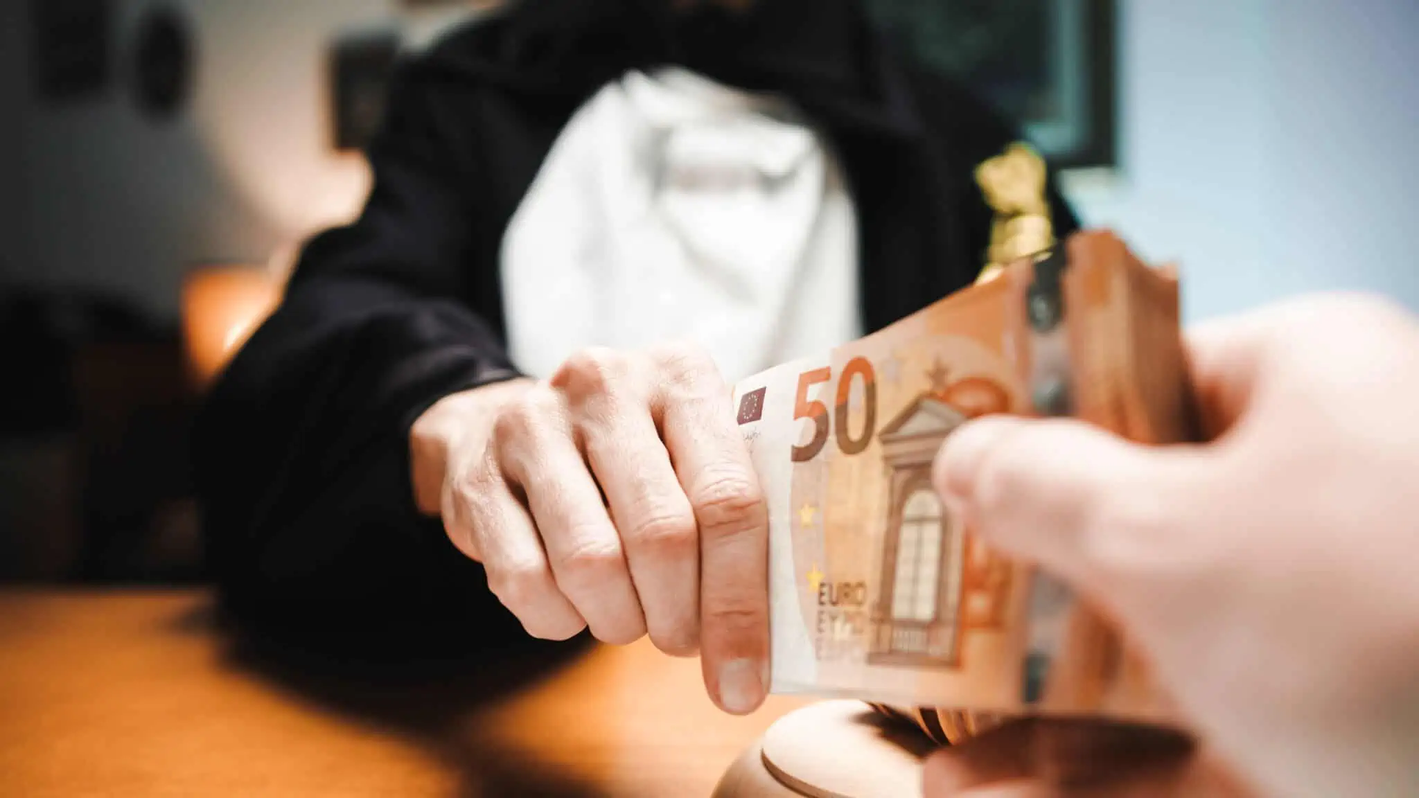 em fundo desfocado duas pessoas puxam pelas pontas de uma nota de 50 euros, aludindo à partilha e divisão do valor de entrada para a casa
