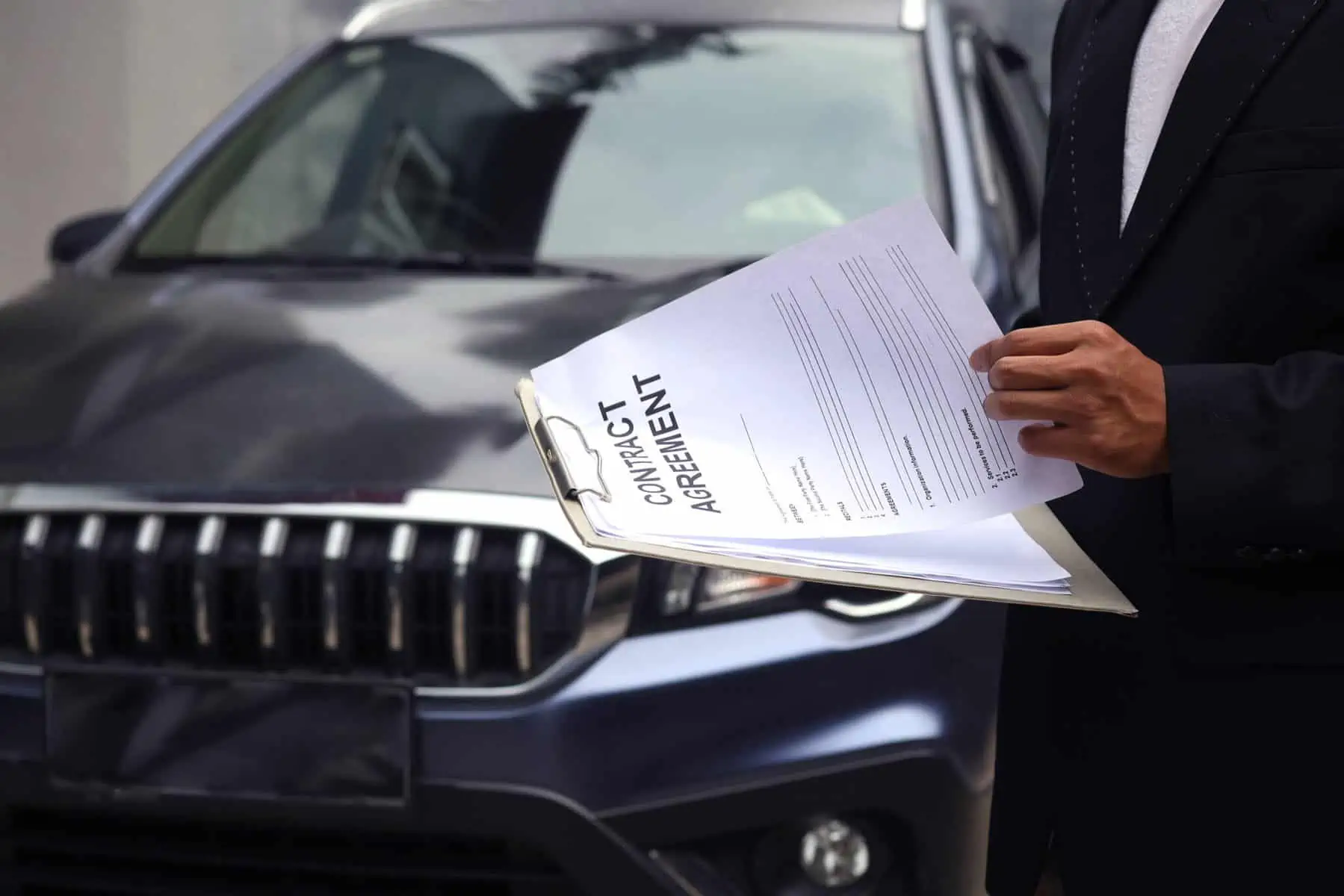 homem consulta acordo, em inglês, junto ao capot de um carro, mostrando a documentação para legalizar esse carro comprado no estrangeiro