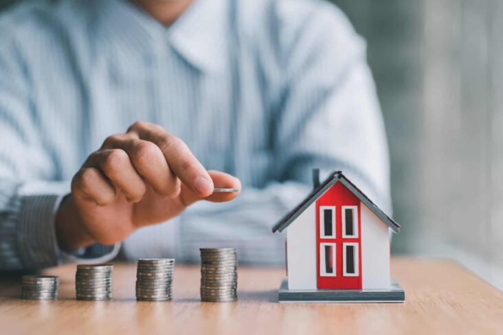 homem a colocar moedas na secretária junto a uma casa a ilustrar como poupar nos seguros do crédito habitação