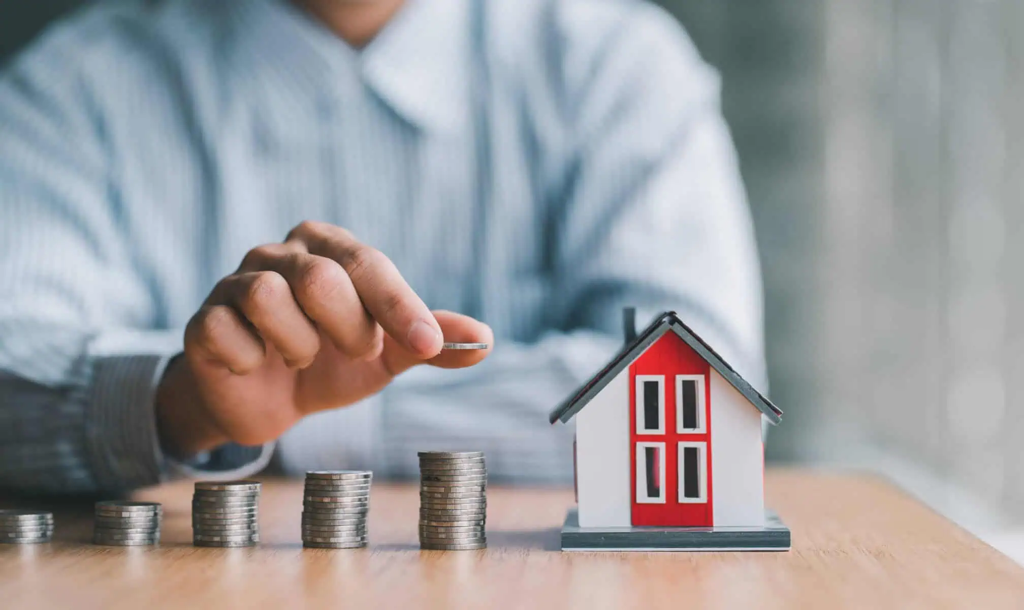 Como posso poupar nos seguros do crédito habitação? homem a colocar moedas na secretária junto a uma casa a ilustrar como poupar nos seguros do crédito habitação