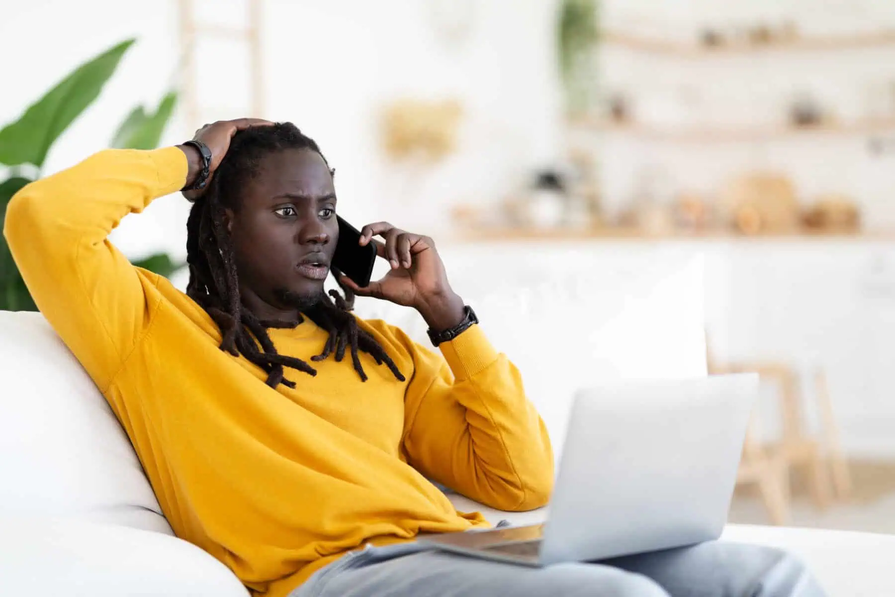 Burlas financeiras: Não forneça códigos enviados para o telemóvel homem sentado no sofá a falar ao telefone com um computador ao colo a ilustrar as novas burlas financeiras realizadas por chamada