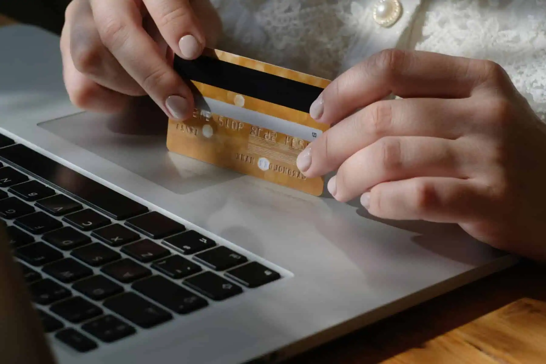 O que acontece ao cancelar um débito direto? mulher com cartão bancário na mão ao pé do computador para cancelar débito direto
