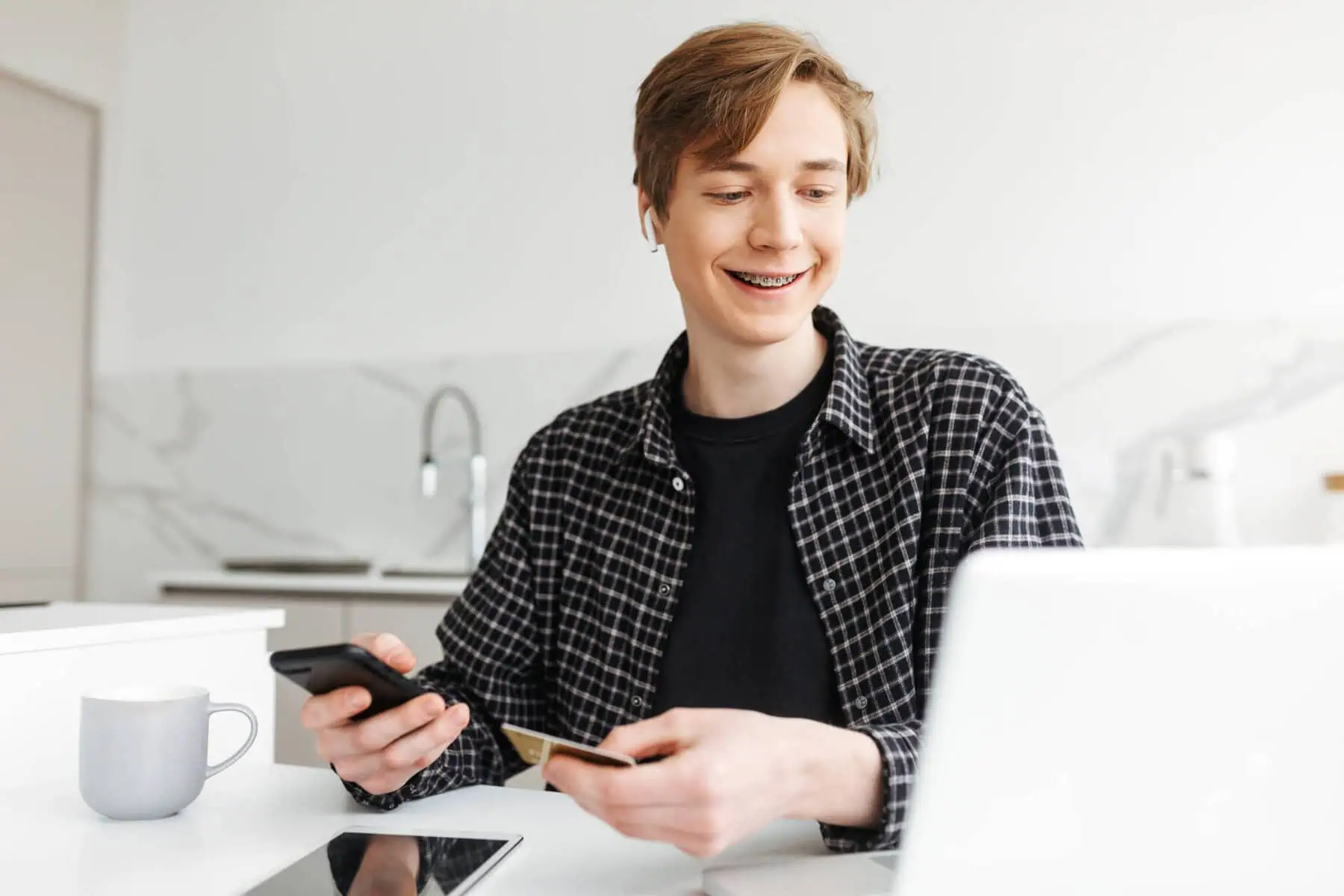 jovem sorridente com um cartão bancário na mão a olhar para o computador a ilustrar como abrir uma conta para um filho