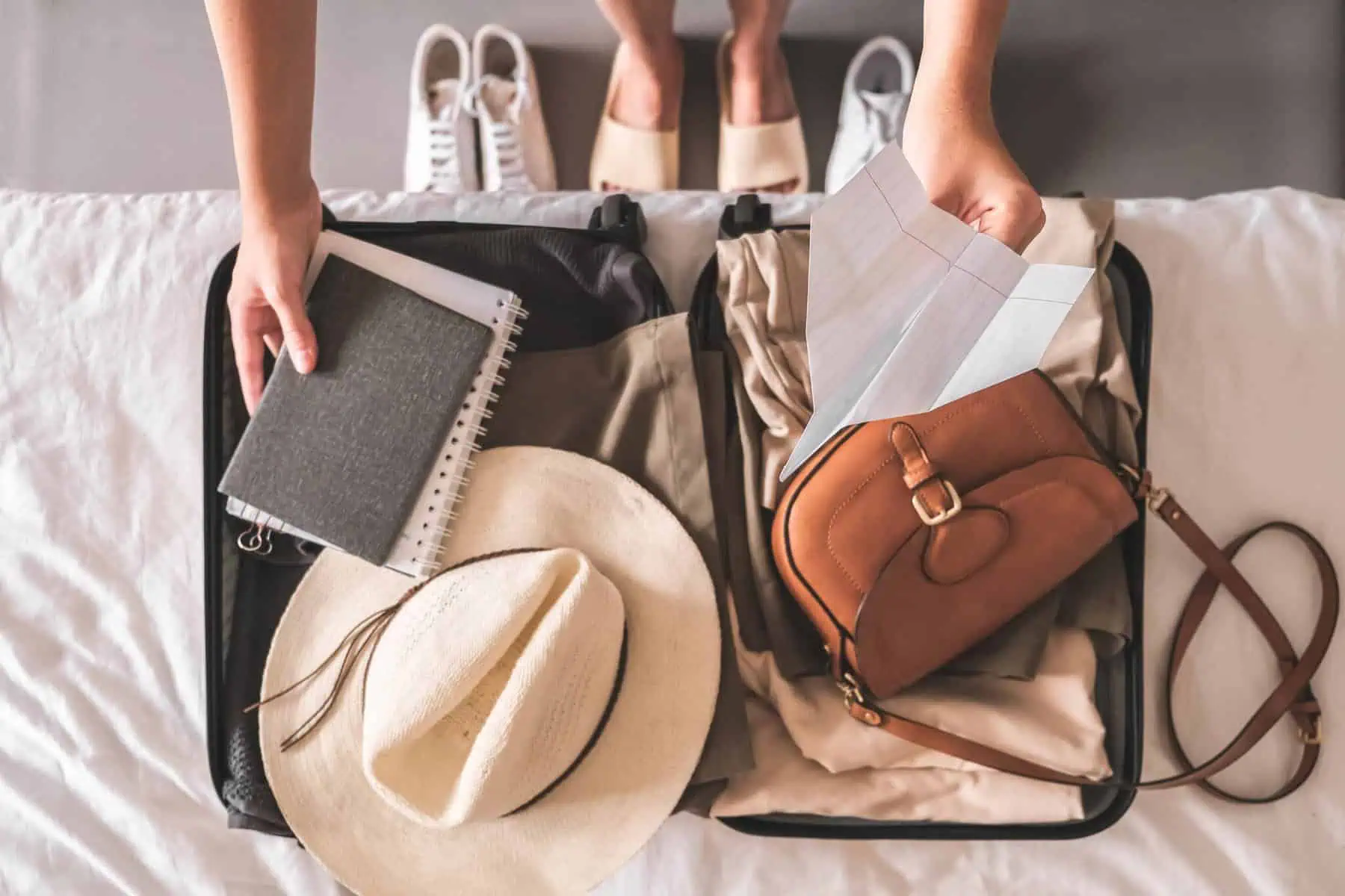 Mala de viagem aberta em cima de uma cama. Dentro encontram-se vários itens, desde roupa a documentos e todo o equipamento para uma viagem de férias