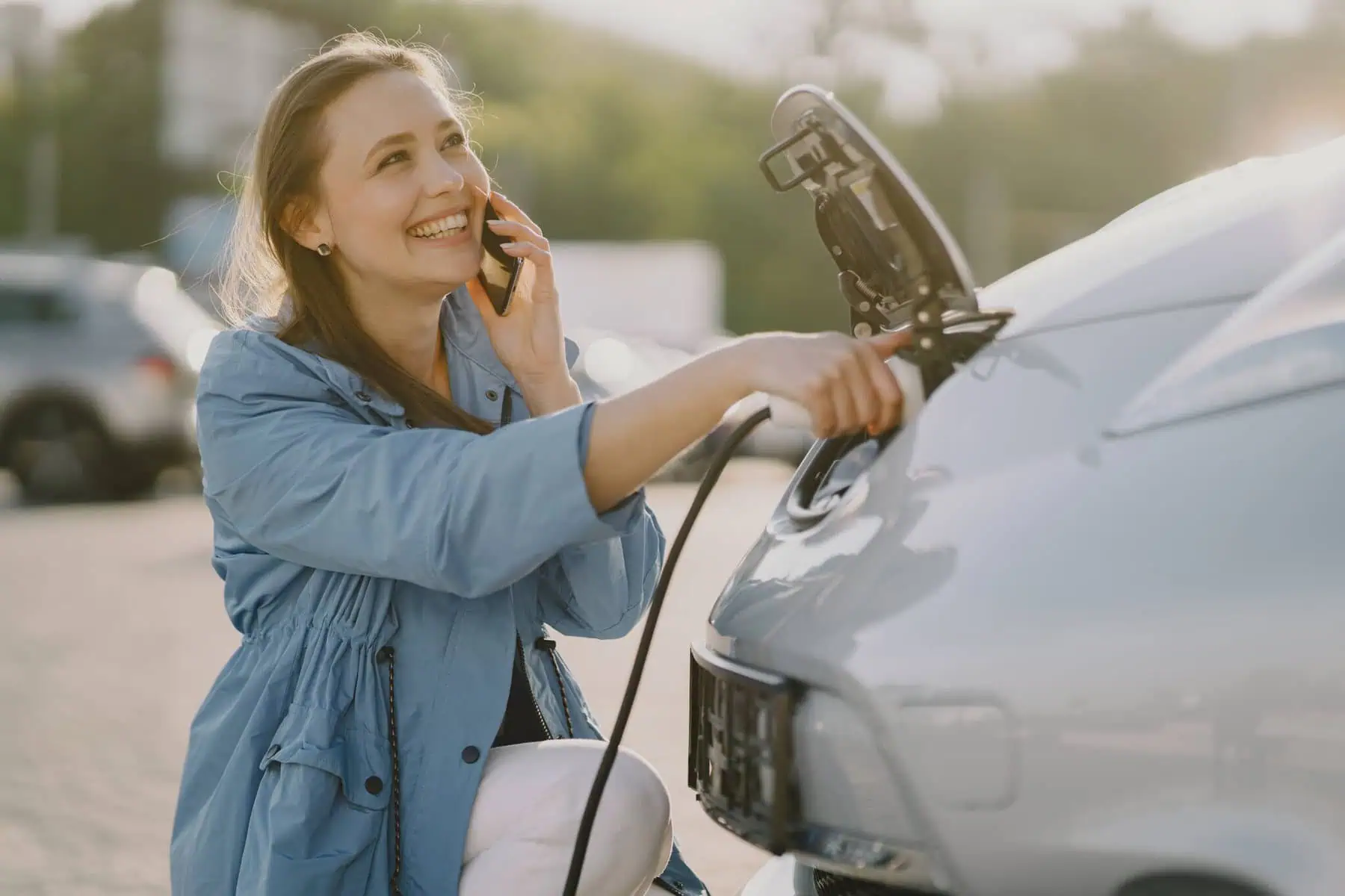 Procura um seguro tão sustentável quanto o seu carro elétrico? Mulher feliz a carregar o seu carro elétrico e a falar com a seguradora