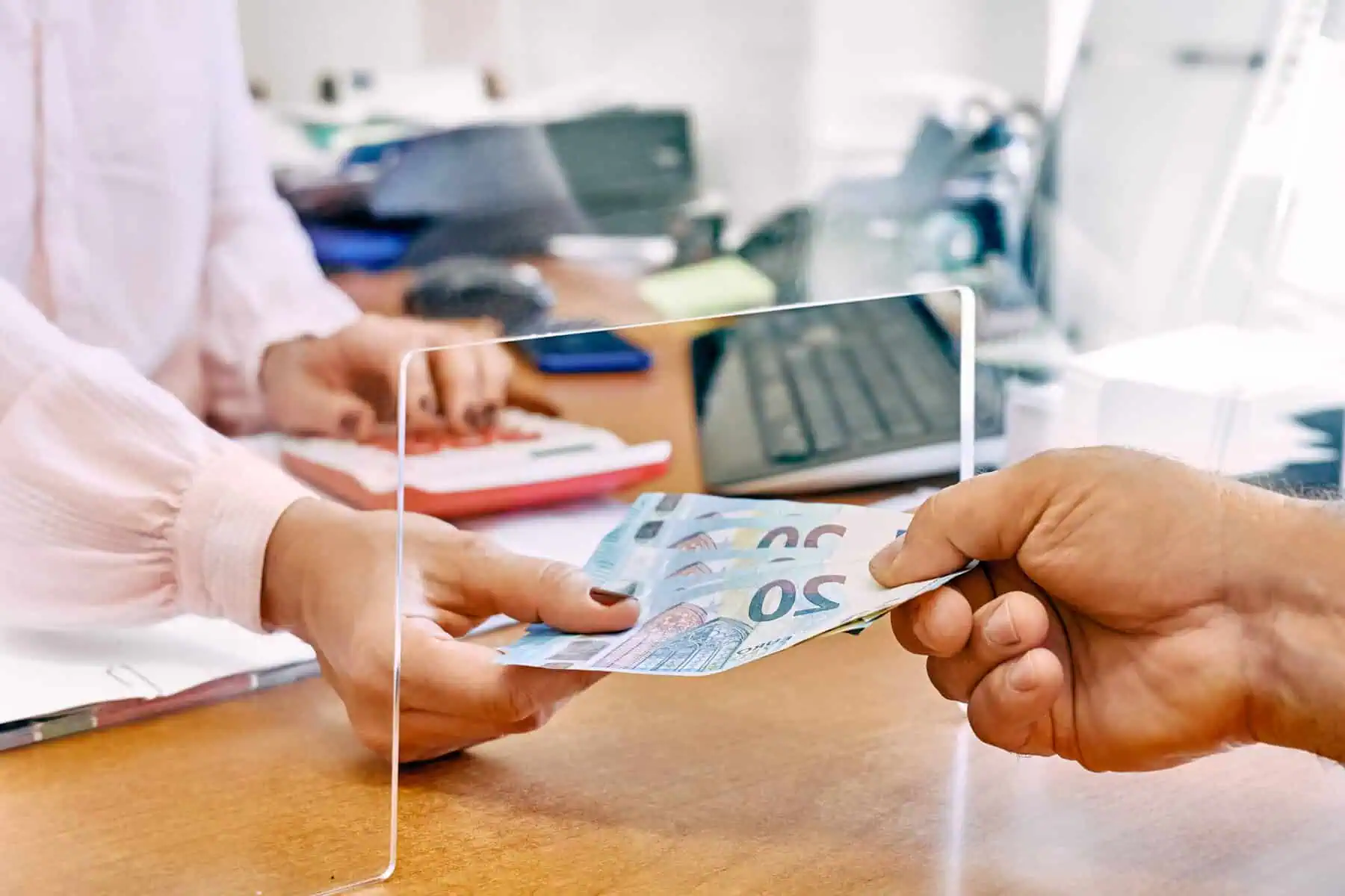 Euro a caminho de valer tanto (ou menos) que 1 dólar. Como mexe na carteira? Mão de homem entrega notas de 20 euros a uma mão de mulher, que está dentro de um guichê de atendimento público