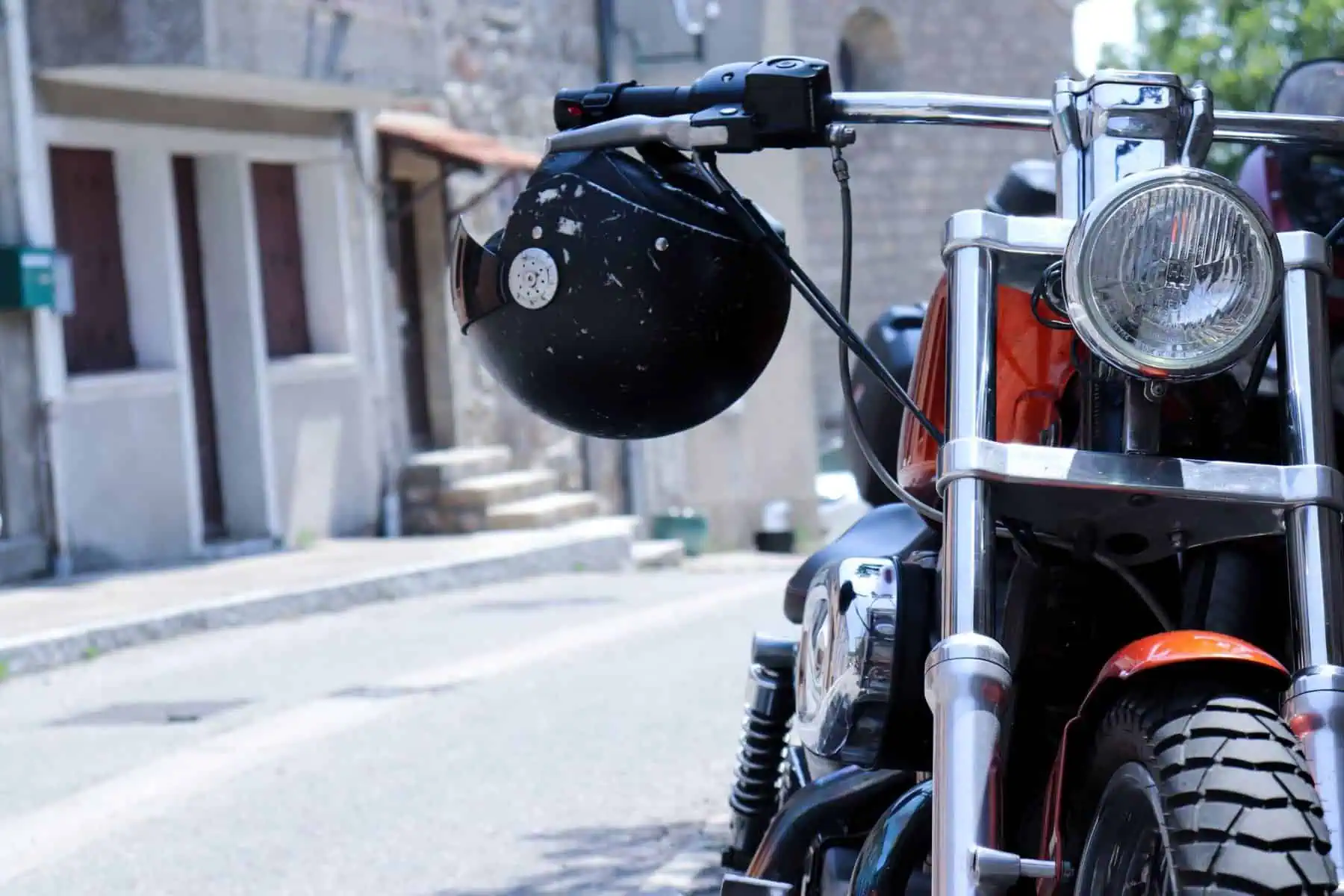 Seguro certo para cada moto: Sabe qual é o seu? Moto estacionada do lado direito da rua. O capacete está pendurado no guiador, numa alusão a um seguro de vida