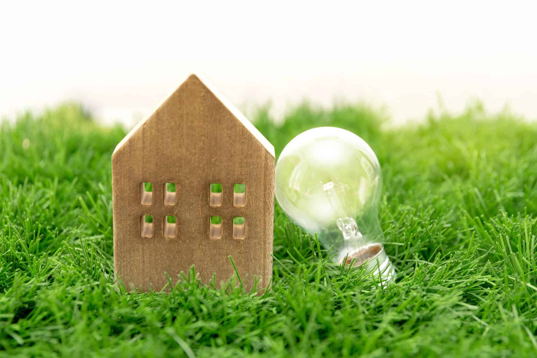 Pequena casa de madeira pousada na relva. Ao seu lado uma lâmpada, numa associação e eficiência energética