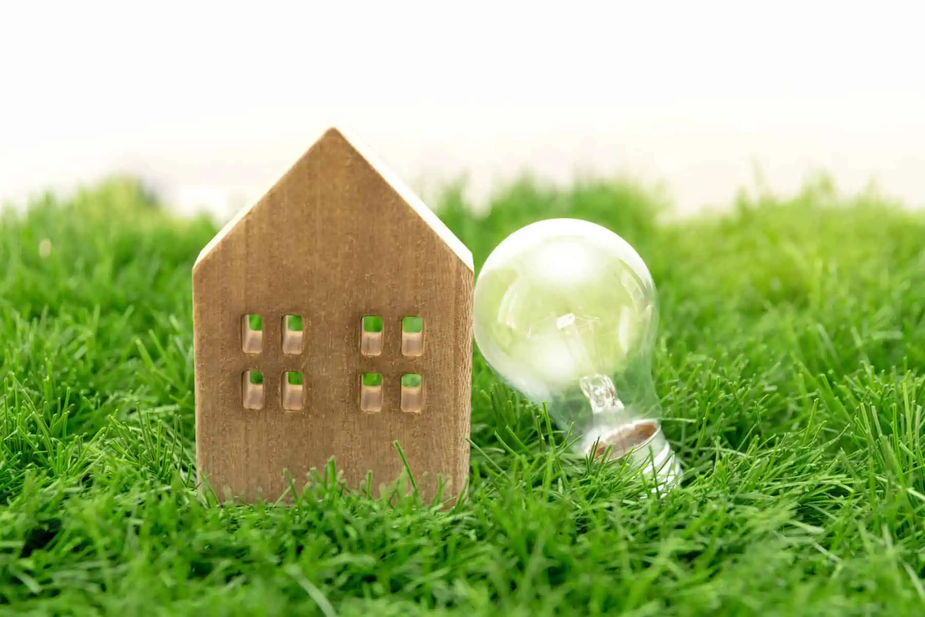 A sustentabilidade na minha casa Pequena casa de madeira pousada na relva. Ao seu lado uma lâmpada, numa associação e eficiência energética