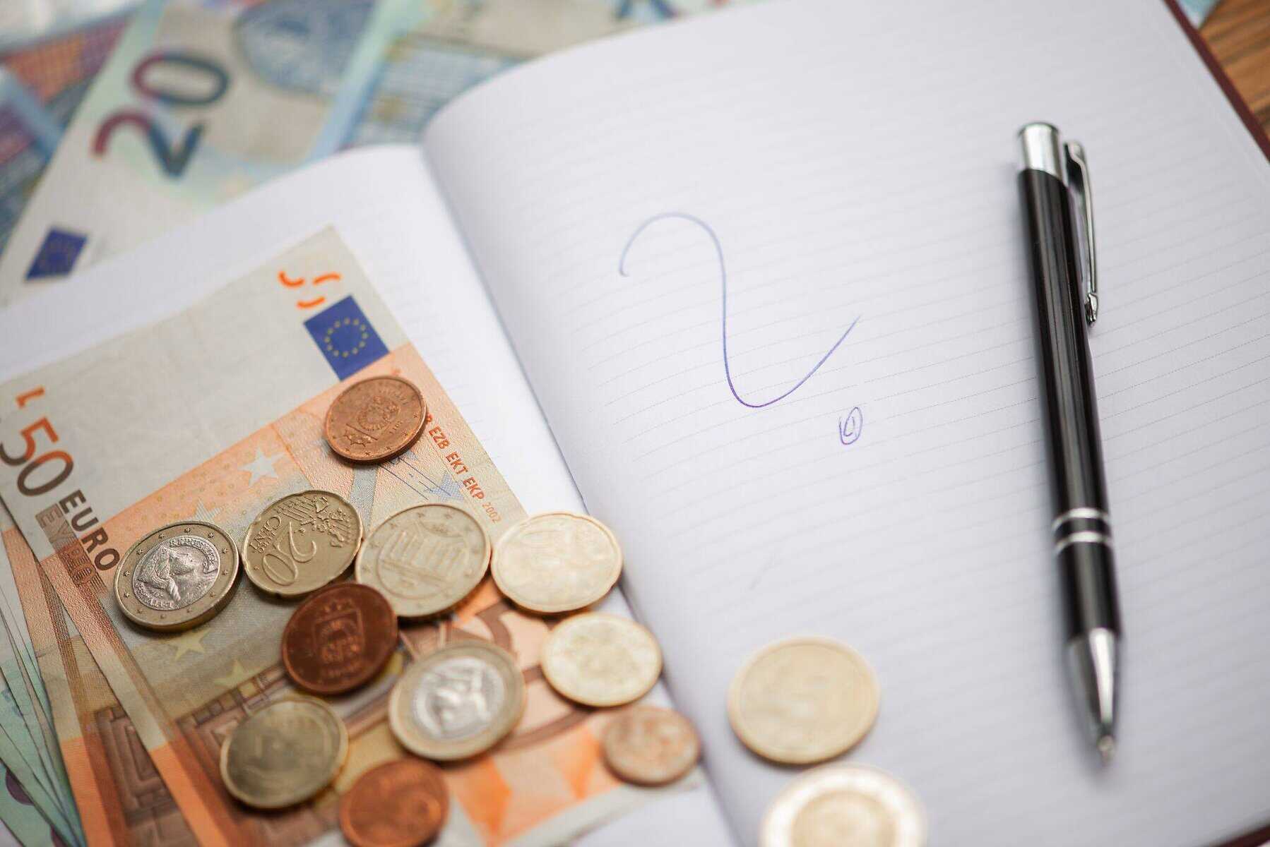 caderno aberto com ponto de interrogação e nota e moedas de euro