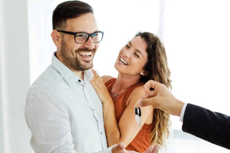 Casal jovem a sorrir e a receber as chaves da sua nova casa, que comprou através do crédito habitação jovem e com a ajuda do Doutor Finanças