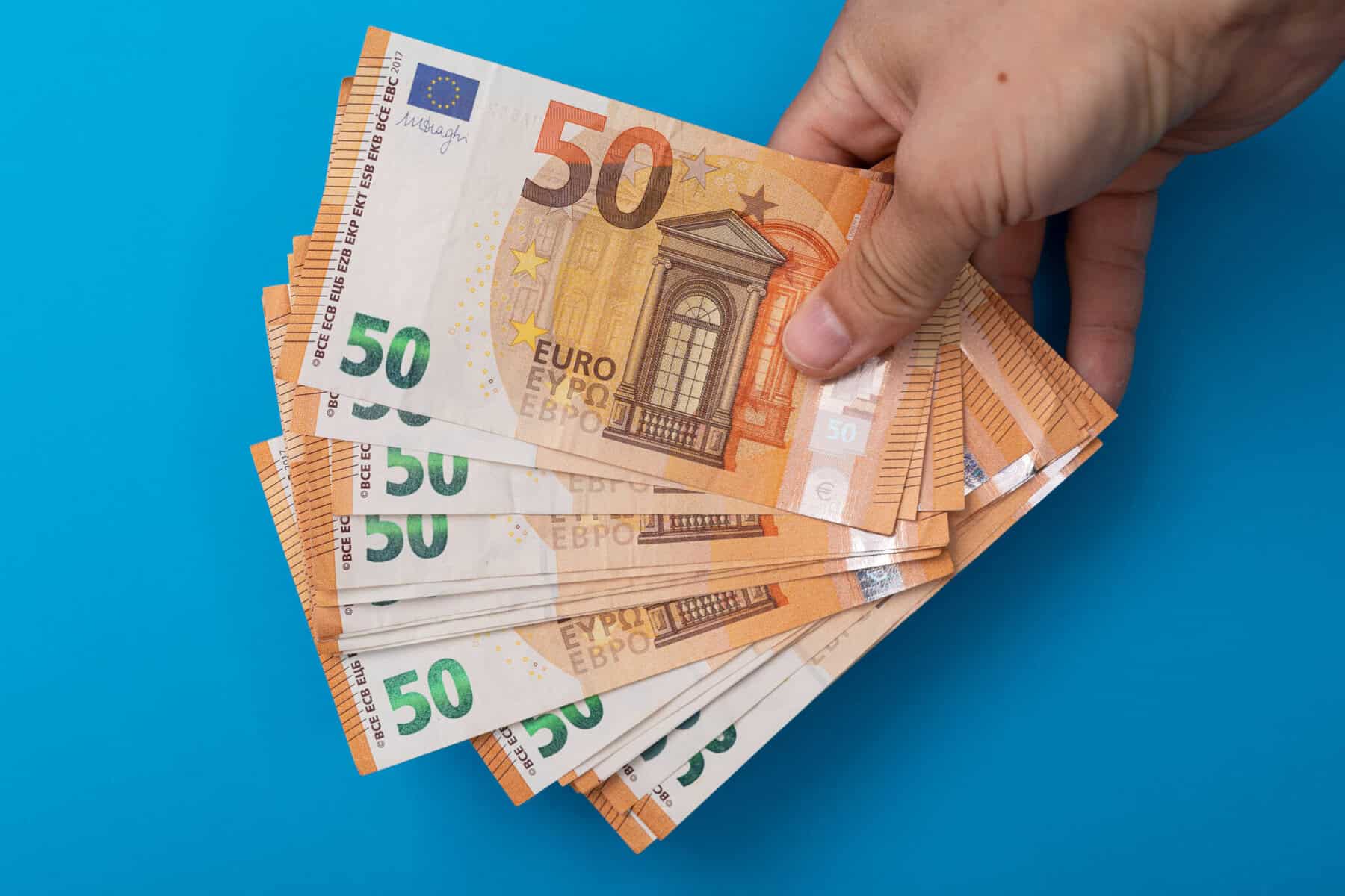 fundo azul com uma mão a segurar notas de 50 euros a ilustrar quanto tempo demora a receber o reembolso de IRS em 2025