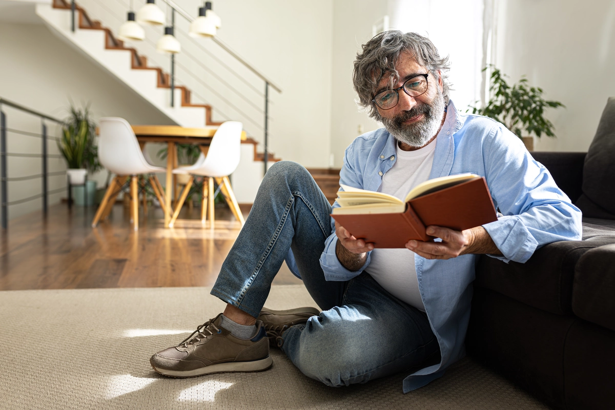 Homem com mais de 50 anos lê um livro na casa comprada