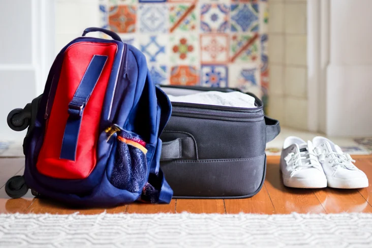 Mochila encostada a mala de viagem aberta, ao lado de umas sapatilhas por calçar