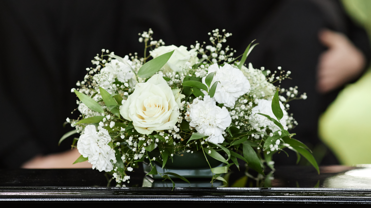 Planos funerários em vida: O que são e como funcionam? Flores brancas sobre um caixão fechado, funeral