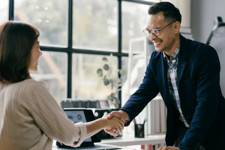 Aperto de mão entre uma entrevistadora e um novo colaborador, após uma entrevista de emprego