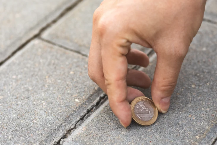 Pessoa a apanhar uma moeda de um euro do chão de tijolo