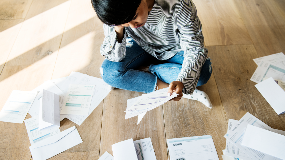 Homem sentado no chão com dívidas espalhadas