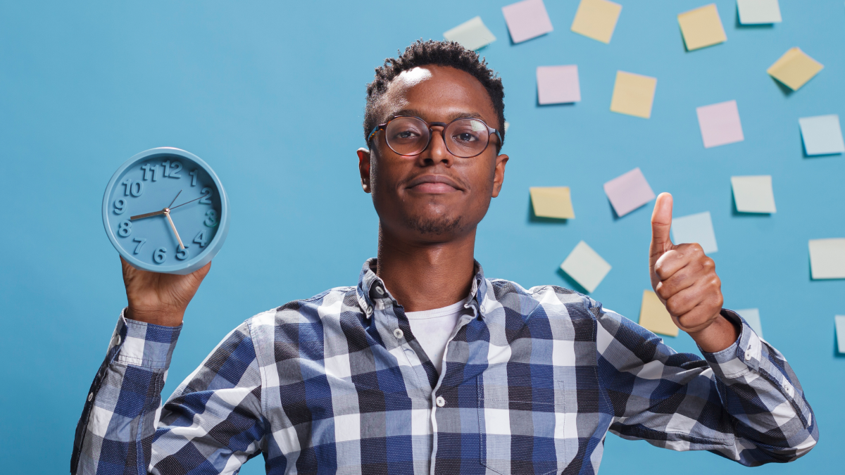 Homem segura em relógio à frente de uma parede azul repleta de notas de trabalho