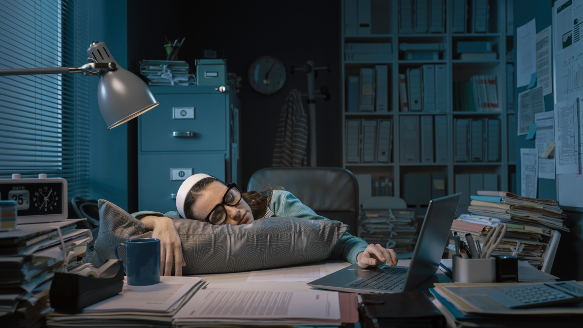 Direito a desligar: Quais as regras? Mulher exausta adormece à secretária no escritório do seu emprego