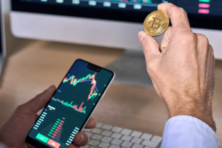 Homem segura em criptomoedas e telemóvel com uma aplicação de investimentos