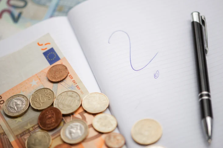 Moedas e notas sobre um caderno aberto com um ponto de interrogação desenhado