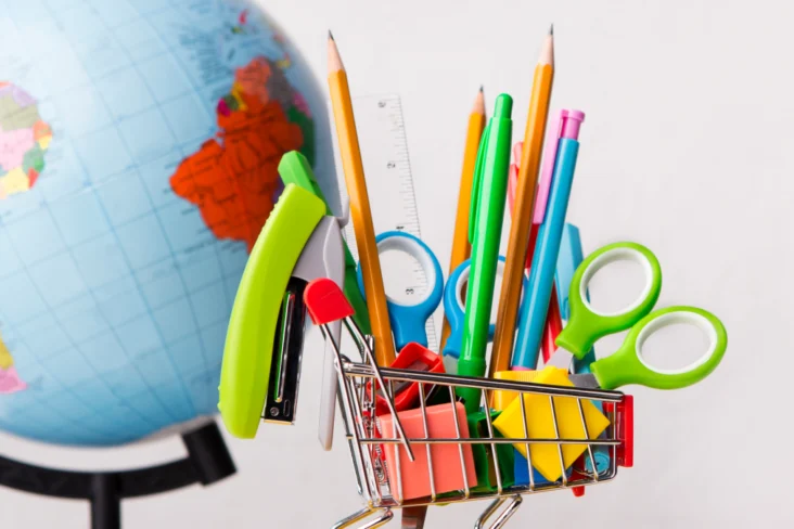 Carrinho de compras miniatura com material escolar à frente de um globo