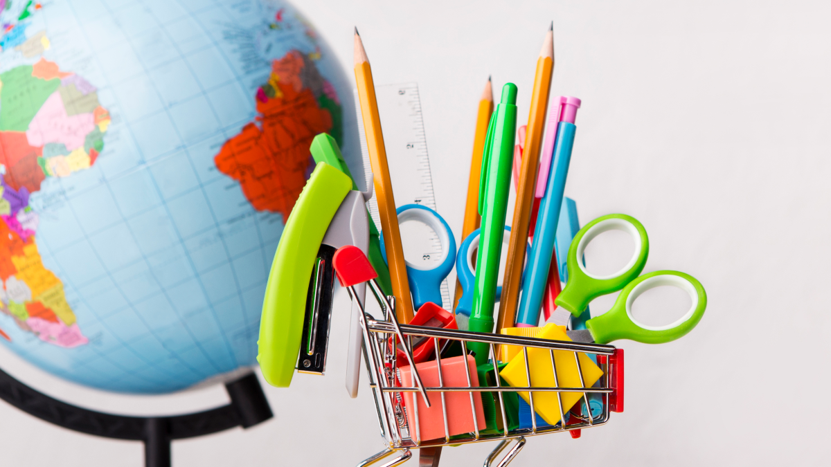 Carrinho de compras miniatura com material escolar à frente de um globo