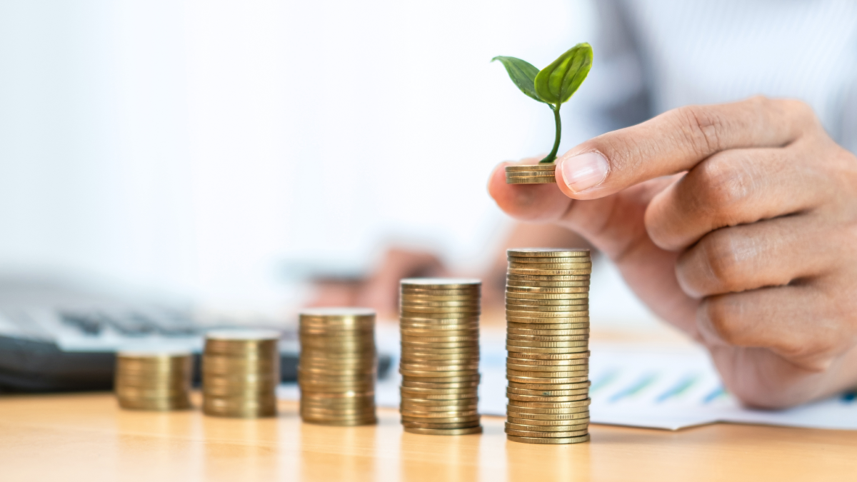 Pessoa empilha moedas em forma de gráfico de barras crescente, com uma planta no topo da moeda