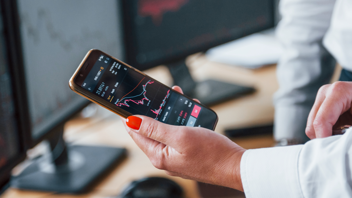 Mulher segura num telemóvel com uma aplicação de investimentos