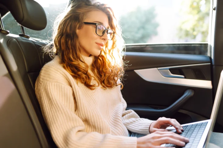 Mulher trabalha remotamente no seu portátil sentada no seu carro após deixar os filhos na escola
