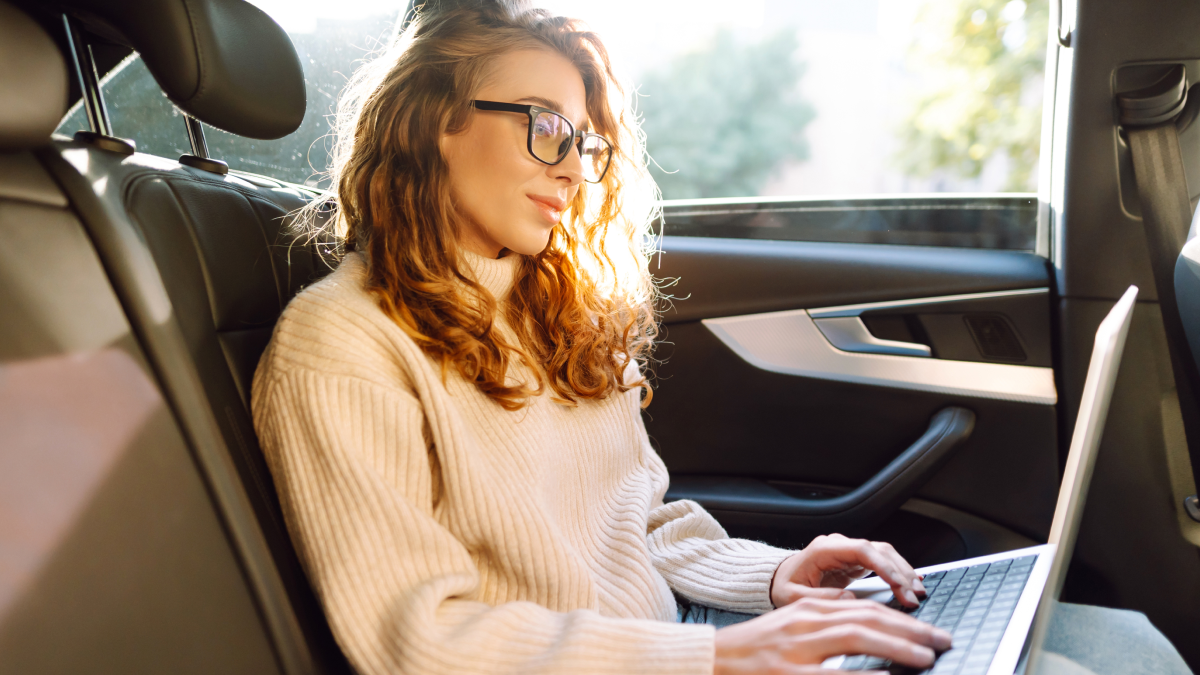 Mulher trabalha remotamente no seu portátil sentada no seu carro após deixar os filhos na escola