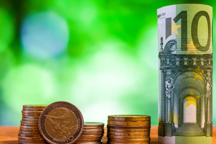 Nota de 100 euros enrolada ao lado de várias moedas empilhadas
