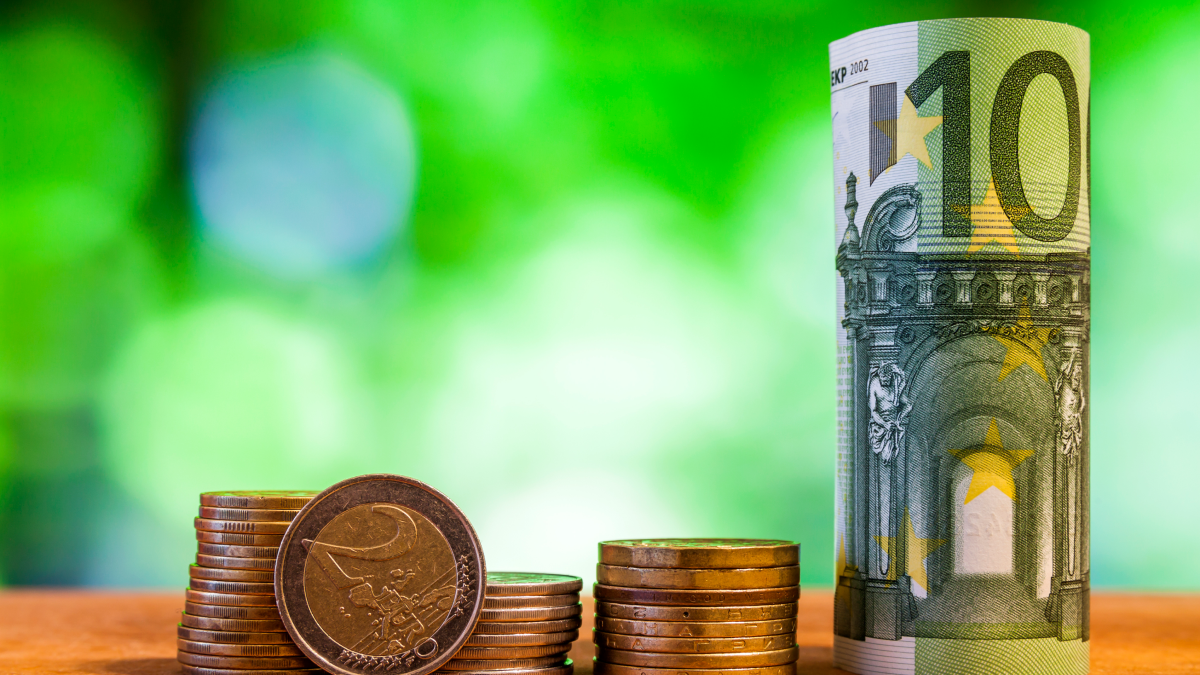 Nota de 100 euros enrolada ao lado de várias moedas empilhadas