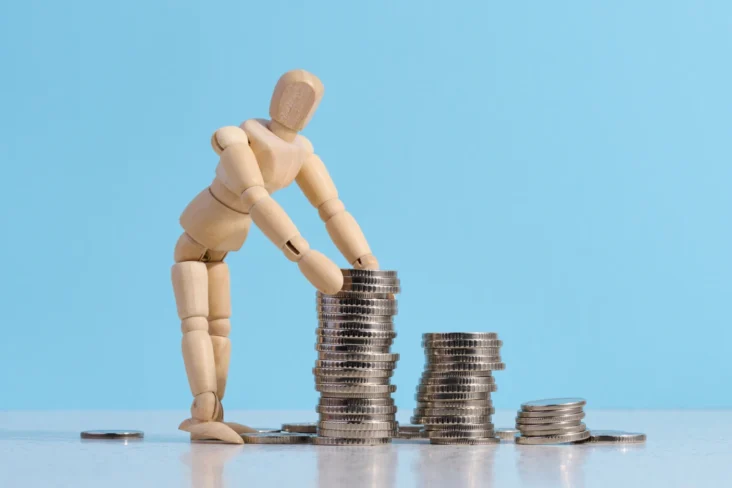 Imagem onde um boneco de madeira constrói uma torre com moedas