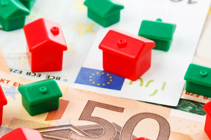 Imagem de várias casinhas de brincar, umas vermelhas outras verdes, sobre notas de euro