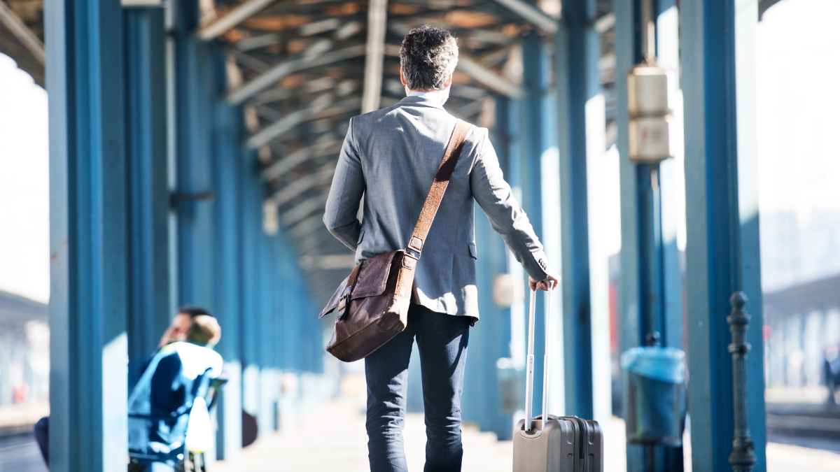 Trabalhadores destacados: Quais os direitos e deveres? Imagem de um homem com uma mala de viagens, de costas, numa estação de comboios