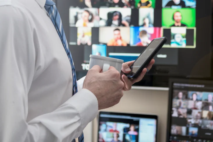 Homem em frente a uma televisão e computador, a segurar num telemóvel