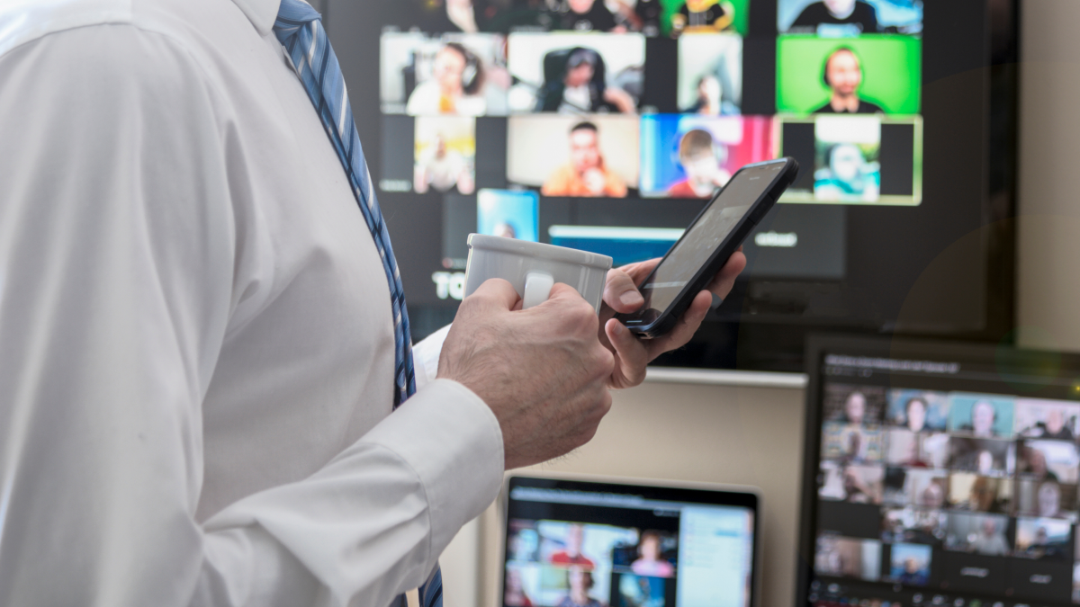 Homem em frente a uma televisão e computador, a segurar num telemóvel