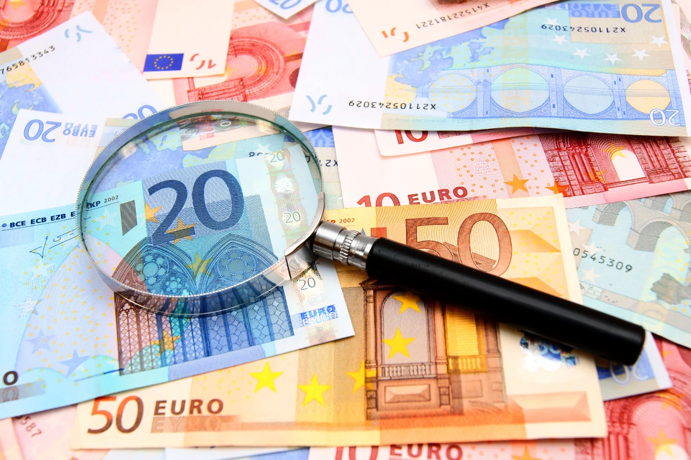 Contas de aforro mais seguras: Validação do NIF e IBAN é obrigatória Imagem de um lupa sobre várias notas de euro