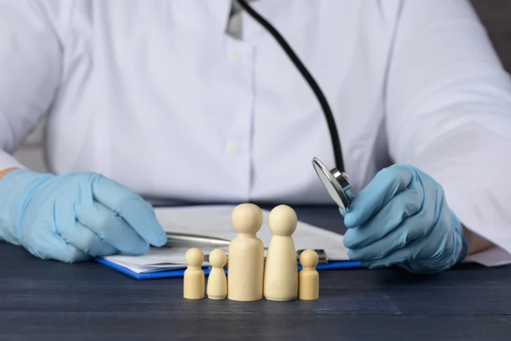 Imagem onde um doutor usa um estetoscópio em brinquedos de madeira que representam uma família