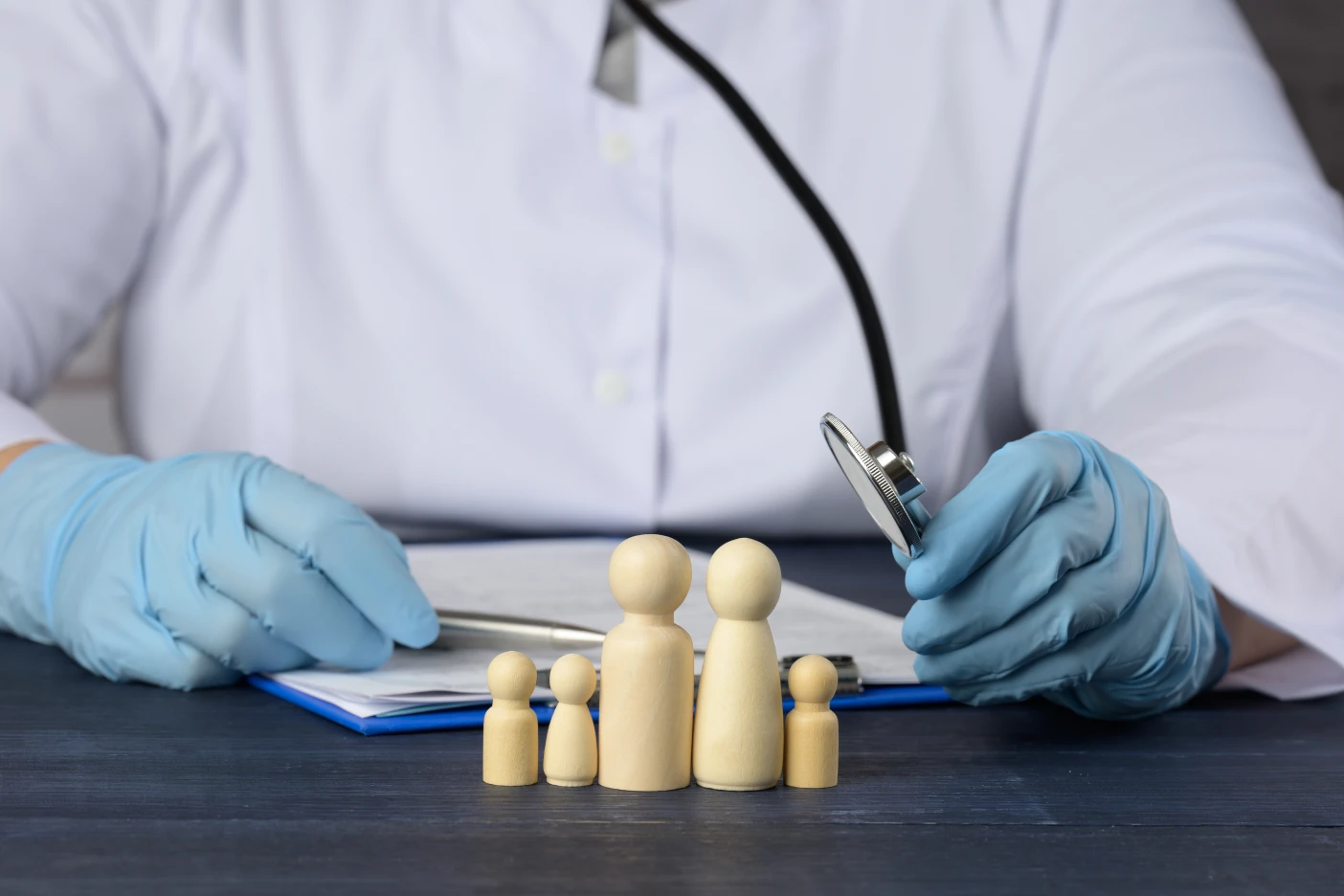 Os 12 erros mais comuns ao contratar um seguro de saúde Imagem onde um doutor usa um estetoscópio em brinquedos de madeira que representam uma família