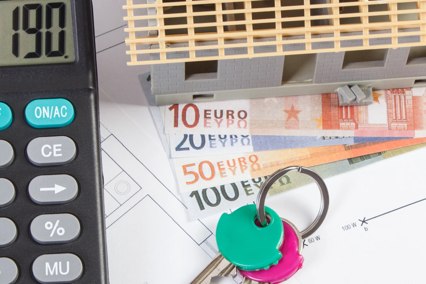 Imagem de uma calculadora, várias notas de euro e umas chaves de casa sobre o diagrama de uma casa
